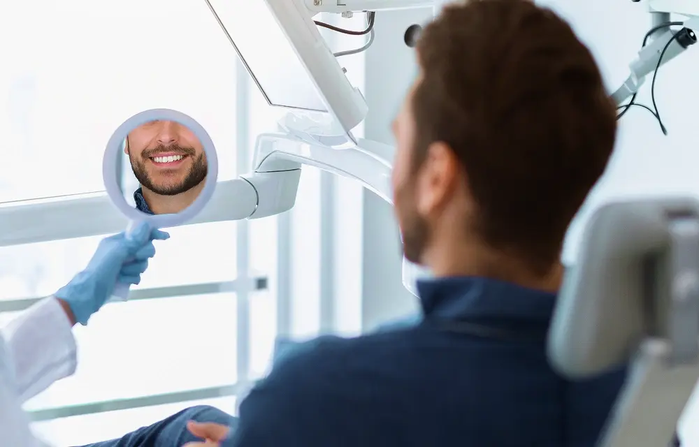 Man seated in a dental treatment chair with his smile reflected in a mirror
